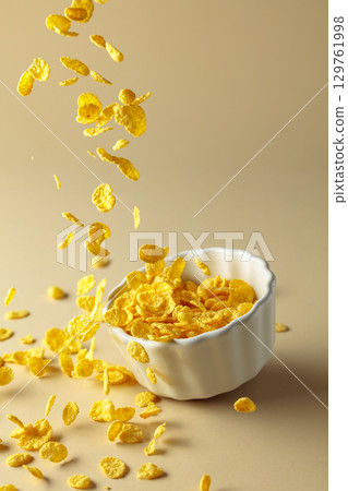 Dry honey cornflakes fall into a ceramic plate. 129761998