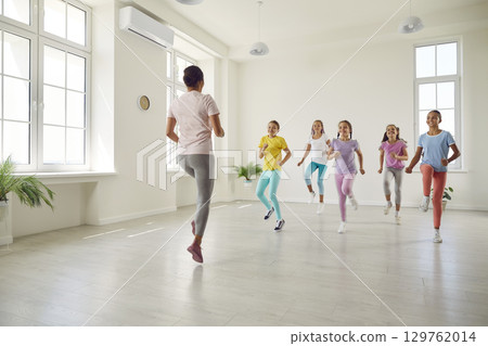 Smiling girls training modern dance moves together in studio with choreographer. Smiling girls training modern dance moves together in studio with choreographer. 129762014