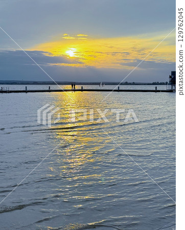 Golden sunset with small clouds over beautiful and calm lake in europe with boat dock 129762045