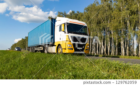 Yellow Blue Truck Driving on Highway Through Forest Landscape and Field Yellow Blue Truck Driving on Highway Through Forest Landscape and Field 129762059