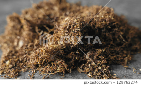 Dry tobacco leaves piled on a gray surface 129762274