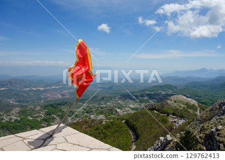 Montenegrin flag flying on top of Mount Lovcen with Cetinje town on background Montenegrin flag flying on top of Mount Lovcen with Cetinje town on background 129762413