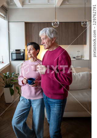 Senior couple watching street through window, talking and drinking tea. Community gossip exchange 129762791