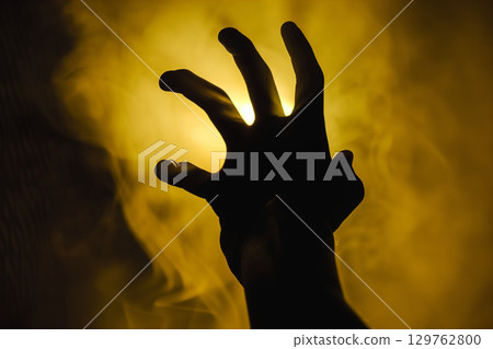 Black hand silhouette and yellow light symbolizing fear. Background material for horror, crisis, and anxiety. 129762800