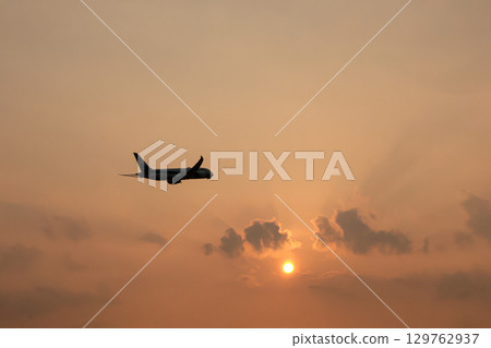 Airplane flying against the setting sun 129762937