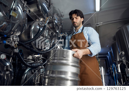 Brewer man is diligently working on a large metal barrel Brewer man is diligently working on a large metal barrel 129763125