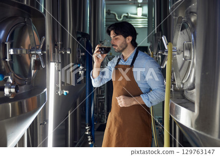 A man wearing an apron is diligently holding a glass of beer A man wearing an apron is diligently holding a glass of beer 129763147