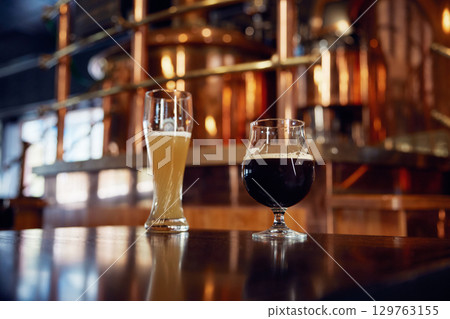 Two cold glasses of beer are comfortably sitting on a bar counter Two cold glasses of beer are comfortably sitting on a bar counter 129763155