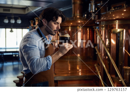 A man is taking in the aroma of a glass of beer in a brewery A man is taking in the aroma of a glass of beer in a brewery 129763157