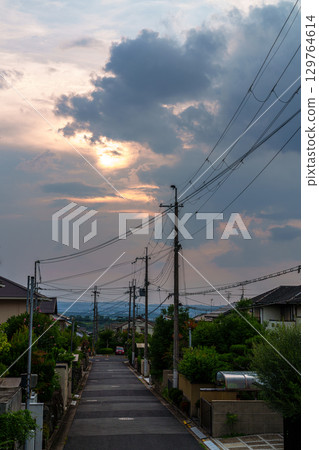 The cityscape illuminated by the setting sun peeking through the clouds. The setting sun paints the sky and city golden. 129764614