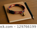 A notebook, pen and cat collar on a desk 129766199