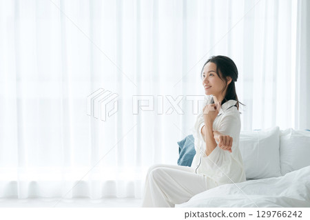 A woman in pajamas waking up in the morning and sitting on her bed 129766242