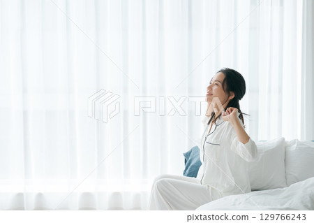 A woman in pajamas waking up in the morning and sitting on her bed 129766243