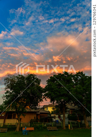 A golden band of clouds appears in the sky east of a residential area, and the park and cityscape are bathed in the colors of the sunset. 129766341