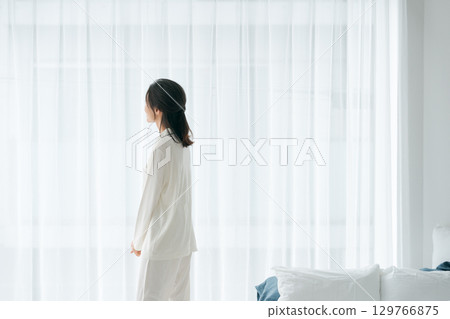A woman in pajamas stretching in the morning sun 129766875