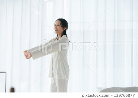 一個穿著睡衣的女人在早晨的陽光下伸展 129766877