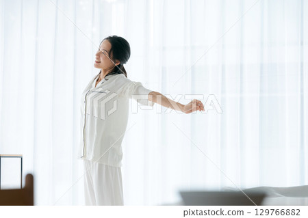 A woman in pajamas stretching in the morning sun 129766882