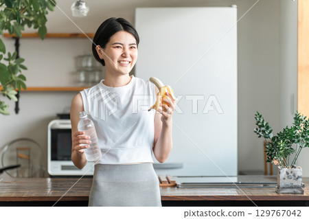 穿著運動服的亞洲年輕女子在廚房吃香蕉（訓練、補充能量、吃點心） 129767042
