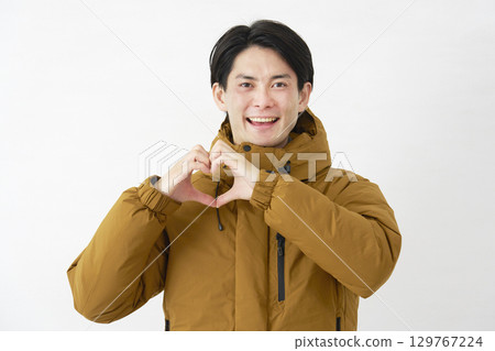 Man wearing down jacket making heart gesture on white background 129767224