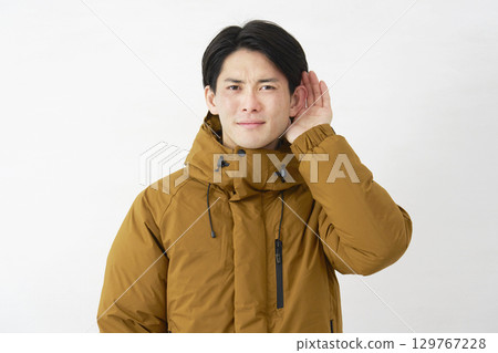 A man wearing a down jacket listening with his hand on his ear, white background A man wearing a down jacket listening with his hand on his ear, white background 129767228
