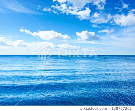 Blue waves reflect the summer sunlight, painting a serene seascape where the ocean meets the horizon under a vast, cloudy sky Blue waves reflect the summer sunlight, painting a serene seascape where the ocean meets the horizon under a vast, cloudy sky 129767261