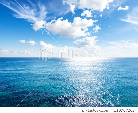 Blue waves reflect the summer sunlight, painting a serene seascape where the ocean meets the horizon under a vast, cloudy sky 129767262