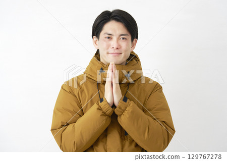 A man wearing a down jacket prays with his hands together, isolated on white background, looking at the camera A man wearing a down jacket prays with his hands together, isolated on white background, looking at the camera 129767278