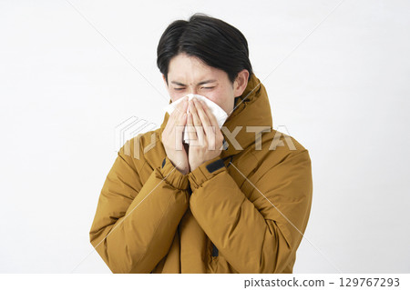 Man wearing a down jacket blowing his nose on white background 129767293