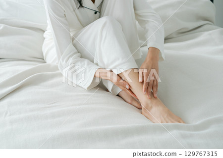 女人坐在床上按摩她的腳 女人坐在床上按摩她的腳 129767315