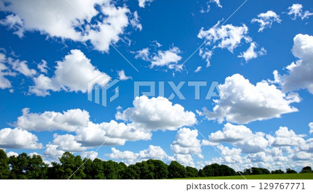 Beautiful blue sky and clouds hover over a vast green meadow, creating a peaceful country landscape on a warm summer day 129767771