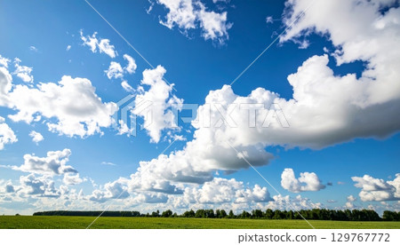 Beautiful blue sky and clouds hover over a vast green meadow, creating a peaceful country landscape on a warm summer day 129767772