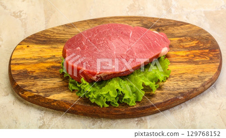 Freshly grilled raw beef steak on a wooden board with a side of vegetables, ready for a gourmet dinner 129768152