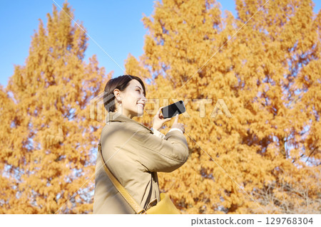 Middle-aged woman taking photos of autumn leaves 129768304