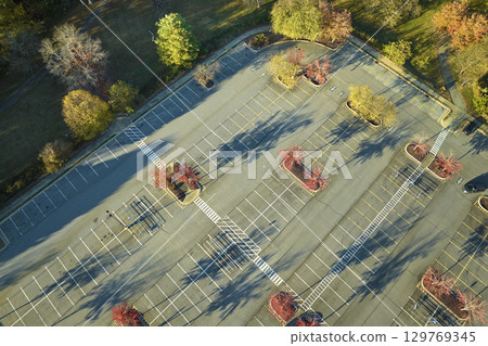 Aerial view of large parking lot with many parked colorful cars. Carpark at supercenter shopping mall with lines and markings for vehicle places and directions 129769345