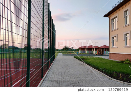 School of preschool building yard with basketball court surrounded with high protective fence. School of preschool building yard with basketball court surrounded with high protective fence. 129769419