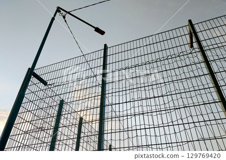 High wire mesh fence in restricted area on blue sky background. 129769420