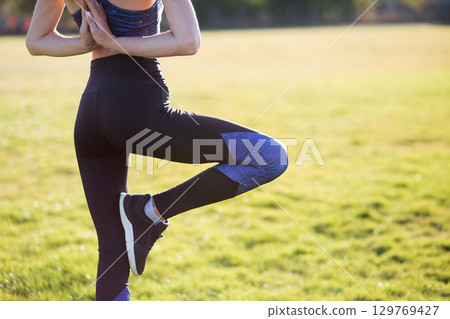 Back view of young girl in yoga position meditates in field at sunrise. 129769427