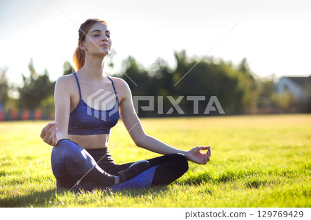 Young sportive woman in yoga position meditates in field at sunrise. Young sportive woman in yoga position meditates in field at sunrise. 129769429