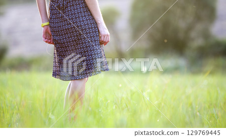 Young woman standing alone on a field with green grass enjoying warm sunset. Young woman standing alone on a field with green grass enjoying warm sunset. 129769445