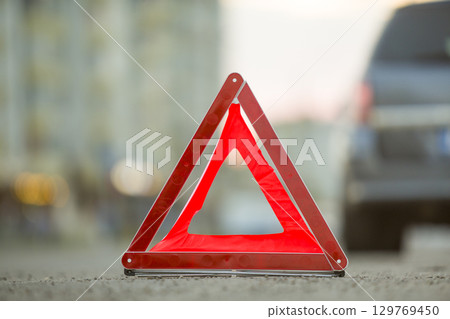 Red emergency triangle stop sign and broken car on a city street. 129769450