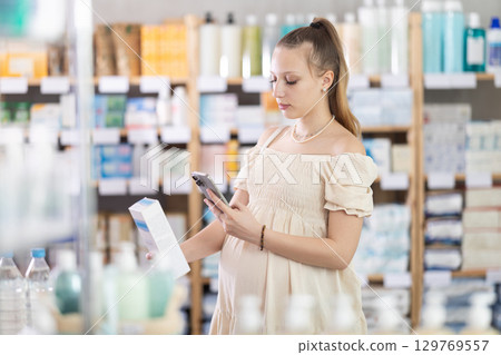Young pregnant woman scanning QR-code on cream in drugstore 129769557