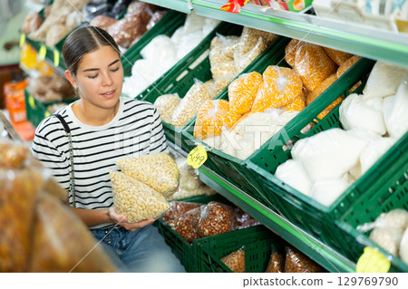 Girl chooses various nuts in the grocery section of supermarket 129769790
