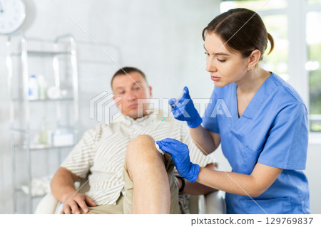 Female doctor performs intra-articular injection treatment of knee bursitis to man patient Female doctor performs intra-articular injection treatment of knee bursitis to man patient 129769837