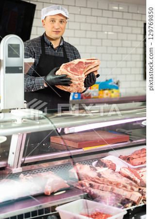 Butcher demonstrating piece of fresh raw veal chop on bone Butcher demonstrating piece of fresh raw veal chop on bone 129769850