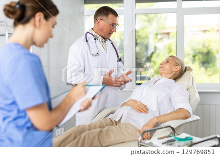 Male beautician giving consultation to woman patient with mirror in aesthetic clinic 129769851