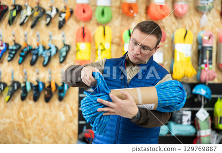 Male tourist chooses and buys climbing rope for an winter hike in tourist equipment store 129769887