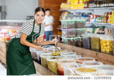 Female supermarket grocery seller offers to buy pickled olives Female supermarket grocery seller offers to buy pickled olives 129769950