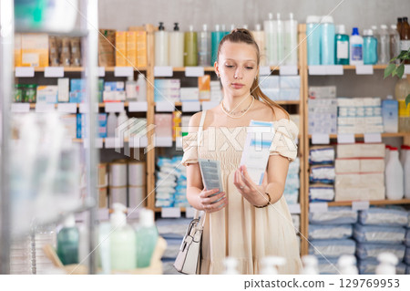 Girl in summer clothes choosing skin cream at drugstore Girl in summer clothes choosing skin cream at drugstore 129769953