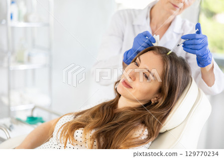 Woman applying scalp injection treatments by male doctor. 129770234