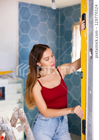 Woman measures deviations from predetermined vertical wall using building level 129770324
